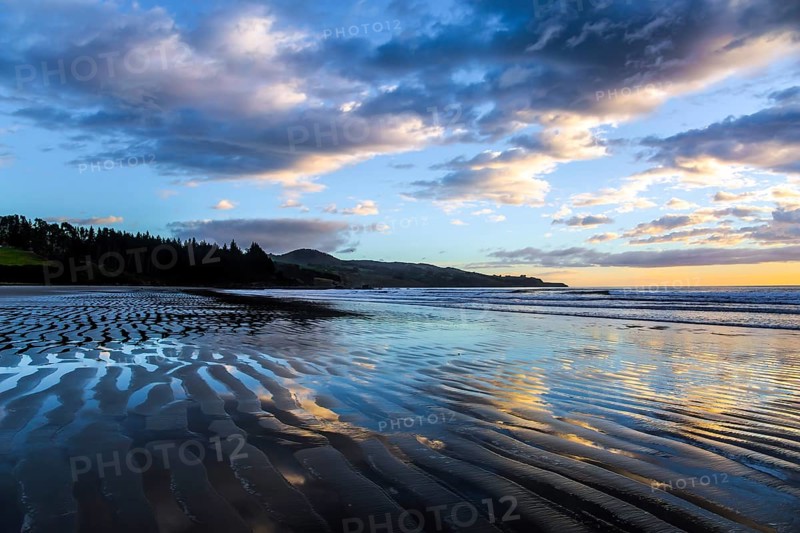 Strips of sand and water left by the ocean tide. Sunrise over the ocean. New Zealand, Pacific Coast. Low tide. The concept of artistic photography. Artistic postal and greeting card
