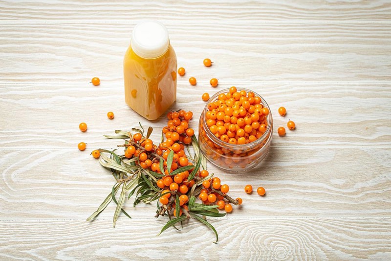 Sea buckthorn healthy drink in bottle, ripe berries in glass jar and branches with leaves top view on white wooden rustic background, great for skin, heart, vessels and immune system, food photography, food photography