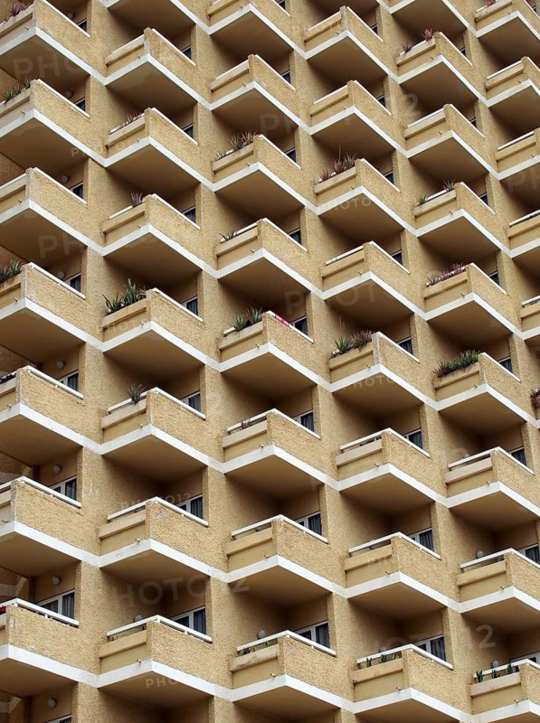 Large highrise modern apartment building with large number of repeating geometric balconies in stone yellow colors