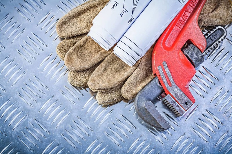 Assortment of pipe wrench engineering drawings leather protective gloves on fluted metal sheet building concept