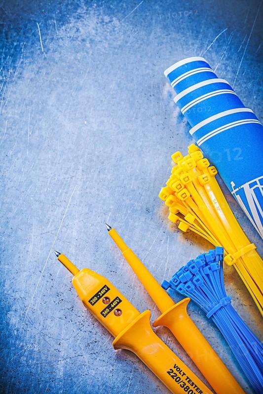Yellow electrical tester self-locking cable ties blue construction plans on metallic background electricity concept