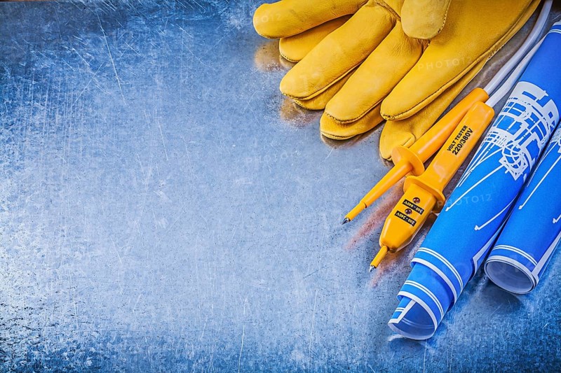 Yellow electrical tester protective gloves blue construction plans on metallic background