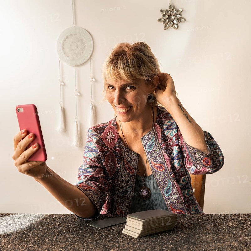 Smiling tarot reader holding her phone in hand while looking at the camera