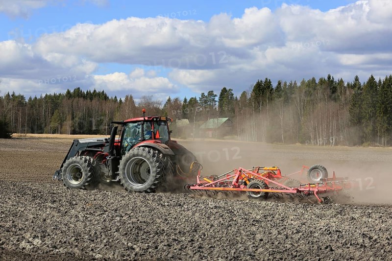 SALO, FINLAND, MAY 7, 2017: Farmer cultivates field with red Valtra tractor and Potila seedbed cultivator on a beautiful day of spring