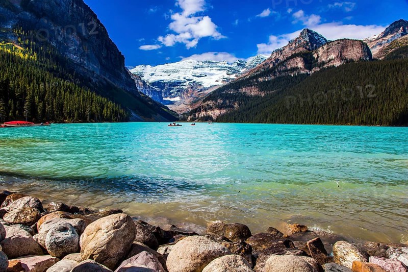 Glacial Lake Louise - the lake with azure water is surrounded by forests and mountains. Rocky Mountains. Red canoes for tourists are moored to the coast. The concept of active and photo tourism