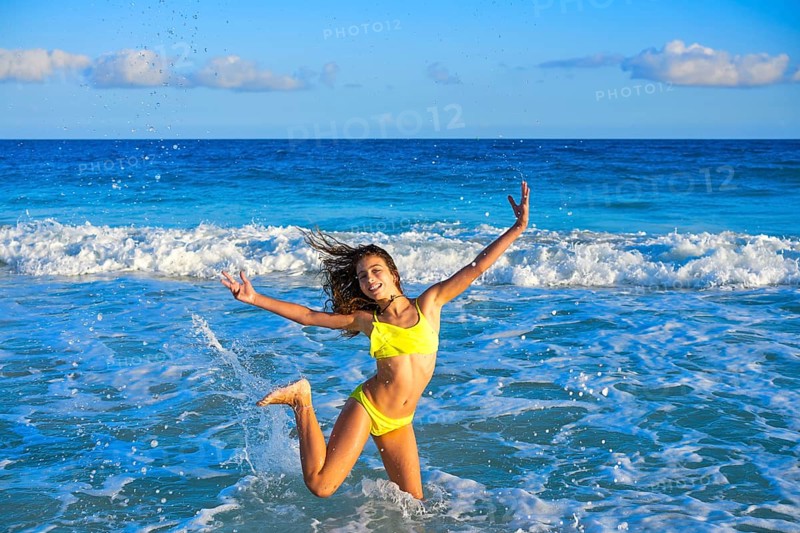 Bikini teen girl jumping happyt in Caribbean sunset beach splashing shore