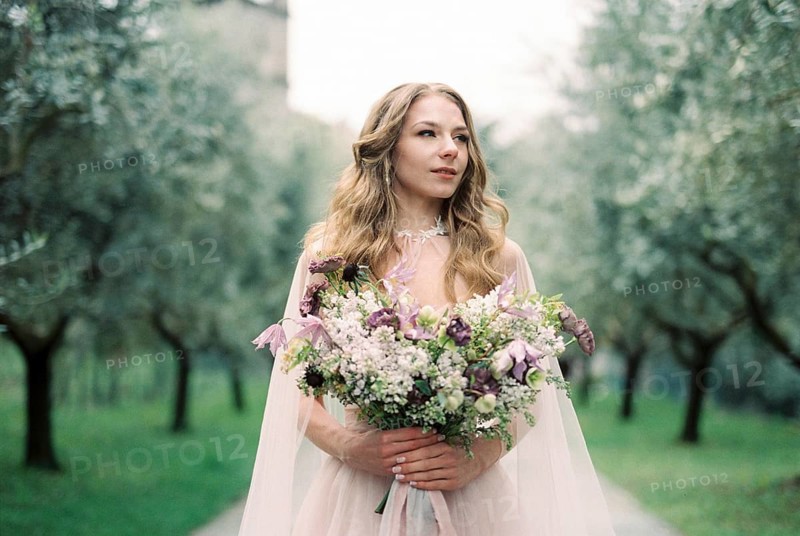 Bride with a bouquet of flowers in an olive grove.