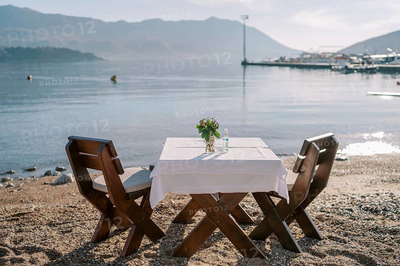 Laid table for two with chairs stands on a sandy beach by the sea.