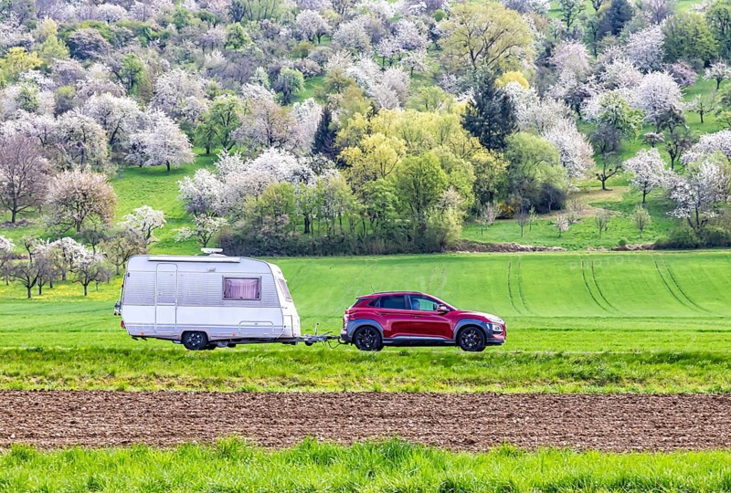 Car with caravan on the Albtrauf in the Lenninger Valley. Blossoming fruit trees in the orchards of the Swabian Alb. Owen, Baden-Württemberg, Germany, Europe