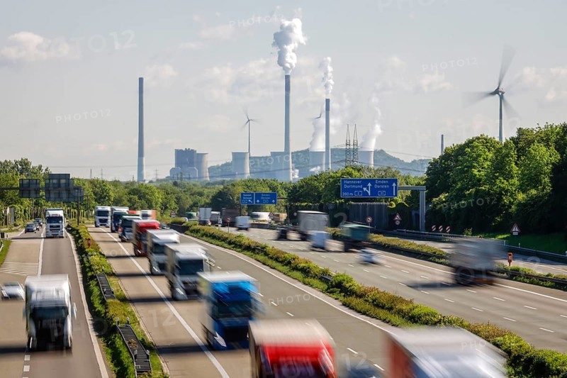 Many lorries driving on the A2 motorway, in the background the Uniper coal-fired power plant Gelsenkirchen Scholven, on the right a wind turbine, Industry and traffic in the Ruhr area, Bottrop, Ruhr area, North Rhine-Westphalia, Germany, Europe