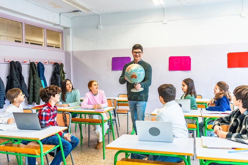 Geography teacher engaging students while holding a globe, fostering learning and understanding in a vibrant classroom environment