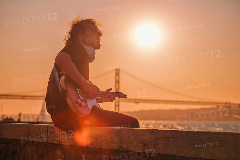 Hipster street musician in black playing electric guitar in the street on sunset