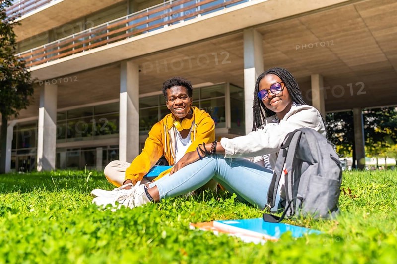Portrait of two african university students relaxed on the grass of the campus smiling at camera