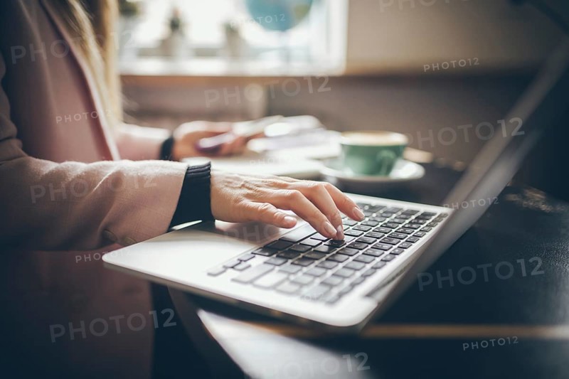 Close-up top view of Caucasian woman's hands Casually dressed student, blogger, writer man working on a laptop holding a phone in his hand, inside the cafe a wooden table and a cup of coffee