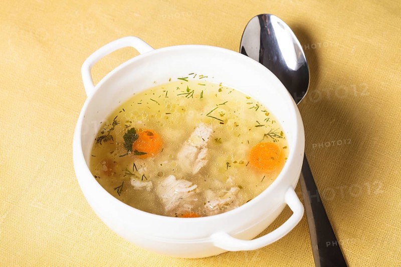 A chicken broth in white ware on the yellow tablecloth