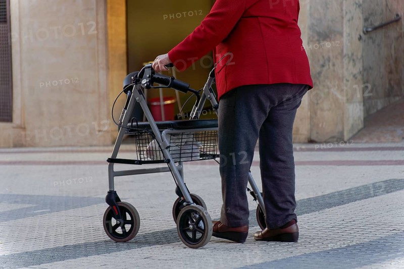 Elderly woman walking along a pedestrian street leaning on her wheeled walker