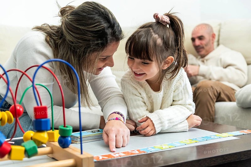 Happy family playing with alphabet puzzle, mother teaching daughter letters, father watching them, educational games for children, early childhood development