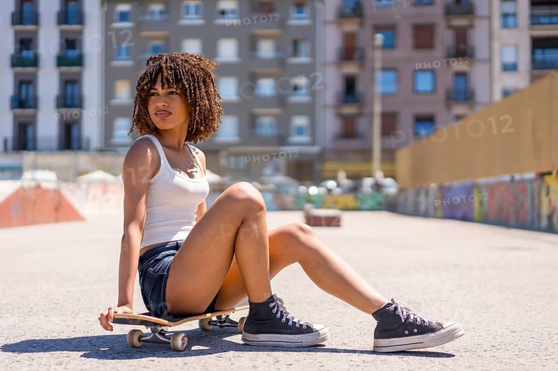 Stylish young woman taking a break, sitting on her skateboard in a skate park, enjoying the urban environment
