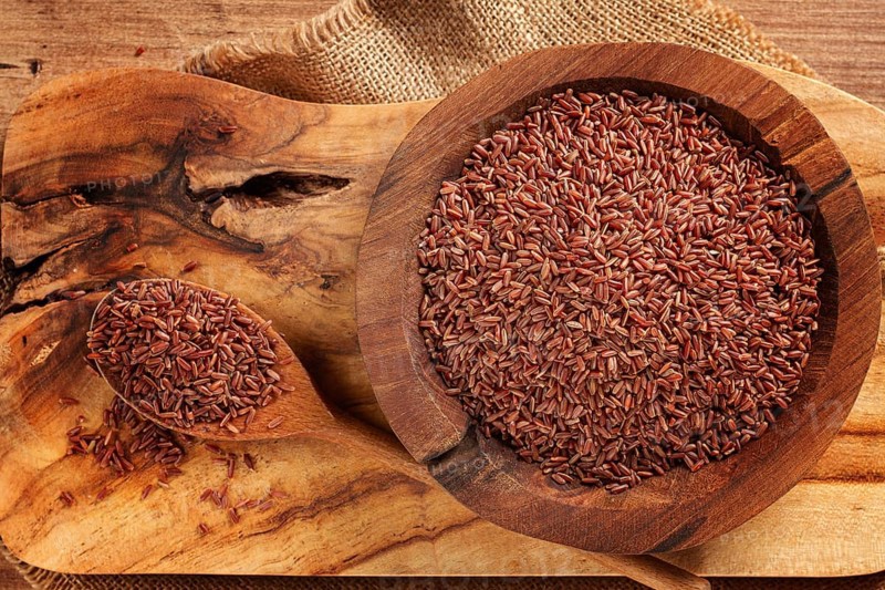 Natural, red rice, in a wooden bowl and spoon on a wooden surface in rustic style, top view