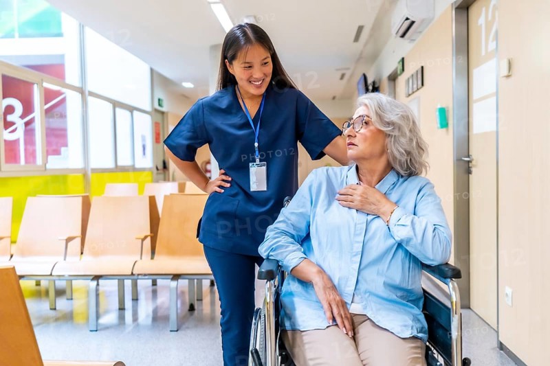 Young nurse assisting and comforting a senior woman in a wheelchair in a hospital waiting room