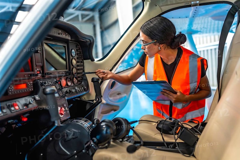 Female aircraft maintenance engineer using checklist while inspecting control panel inside cockpit of light aircraft