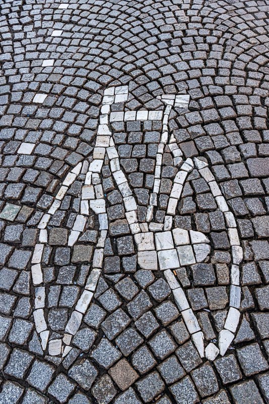 A bicycle mosaic is skilfully integrated into a street of paving stones, traffic, bicycle road, street