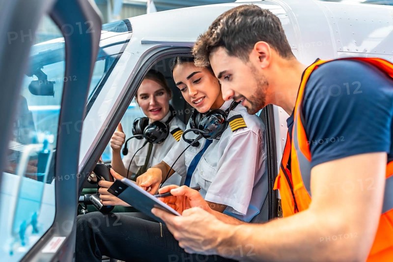 Airplane maintenance engineer briefing two smiling female pilots showing thumbs up sitting inside the cockpit