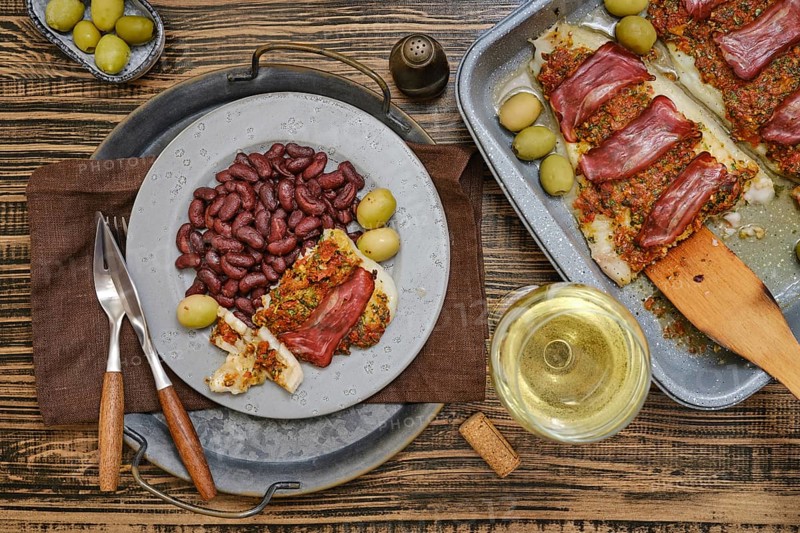 A delectable plate of fish topped with herbs and meat is presented alongside kidney beans and green olives