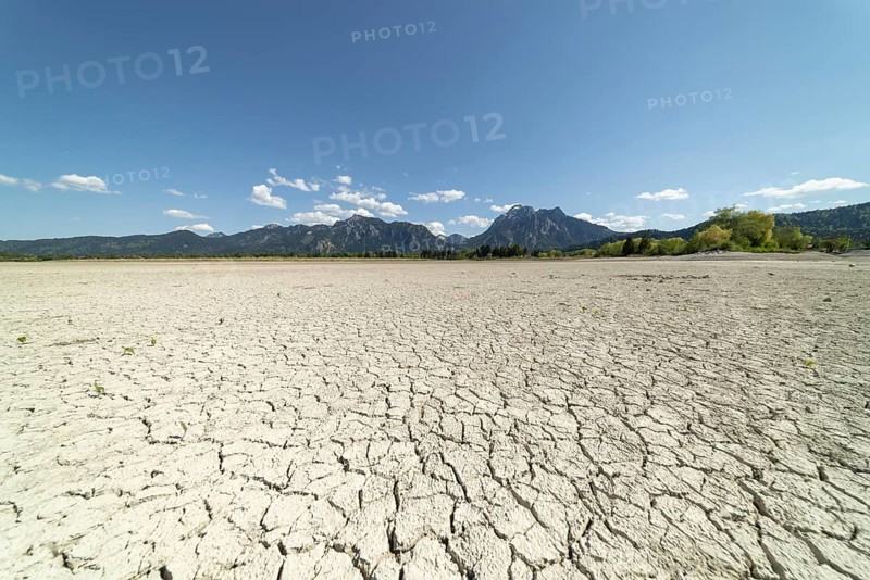 Cracked, dried out ground, waterless Forggensee in spring, behind it Tegelberg massif and Säuling, Ammergau Alps, near Füssen, Ostallgäu, Bavaria, Germany, Europe