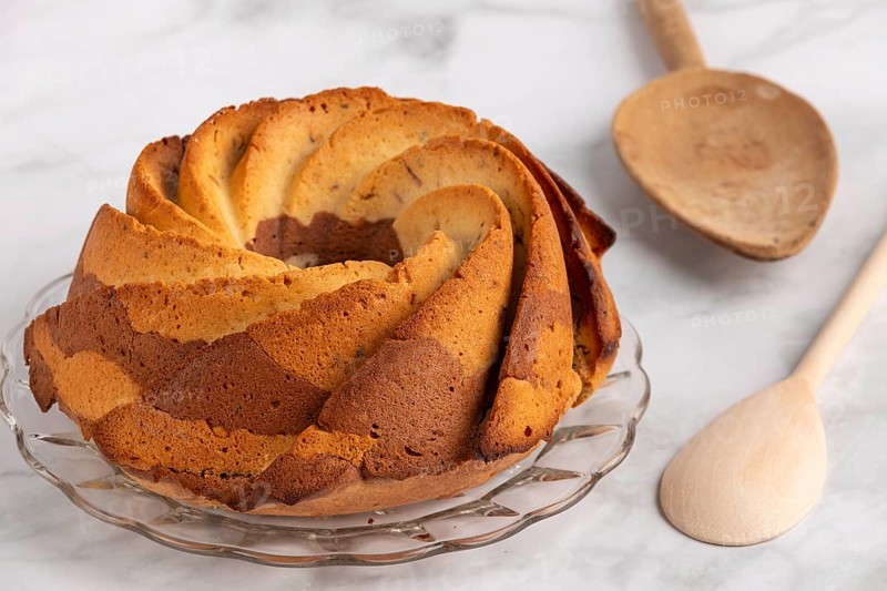 Fresh marble bundt cake, cake next to a rustic wooden spoon on a light-coloured background