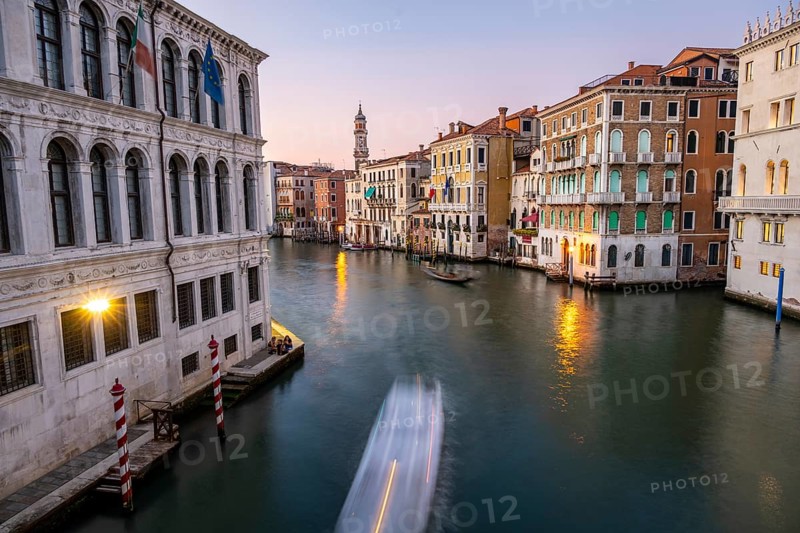 View of the Grand Canal with gondoliers at sunset, picturesque evening mood with illuminated palazzos on the canal and church tower of the Chiesa Parrocchiale dei Santi Apostoli, long exposure, view from the Rialto Bridge, Venice, Veneto, Italy, Europe