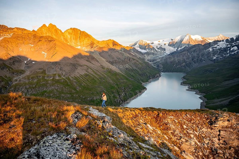 Mountaineer on the summit of Mont de la Blana, alpenglow at sunset, view of a blue mountain lake, Lac des Dix reservoir, behind mountain peak Mont Blanc de Cheilon with glacier, Hérménence, Valais Alps, Valais, Switzerland, Europe