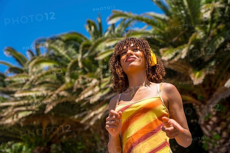Tourist enjoying music while wearing headphones in a vibrant tropical paradise, surrounded by swaying palm trees under a sunny blue sky
