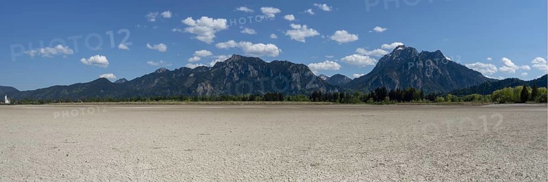 Cracked, dried out ground, waterless Forggensee in spring, behind it Tegelberg massif and Säuling, Ammergau Alps, near Füssen, Ostallgäu, Bavaria, Germany, Europe