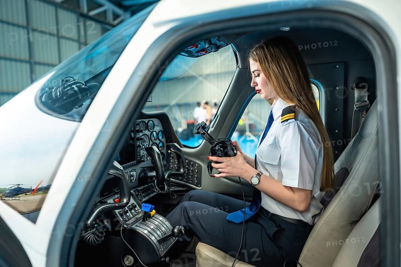 Female pilot sitting in the cockpit of a small airplane and preparing her headset, ready for takeoff