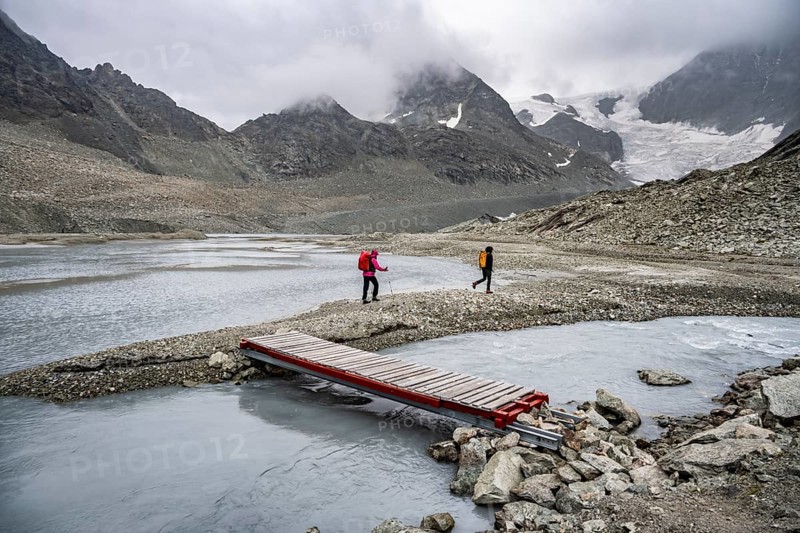 Mountaineers at a makeshift bridge over a stream, glacier river at the Glacier de Cheilon, in the background mountain peak Mont Blanc de Cheilon in clouds, Valais, Western Alps Switzerland