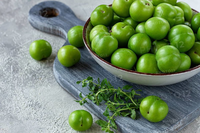 Tkemali, green cherry plum, in a bowl, on a gray table, top view, natural light, no people