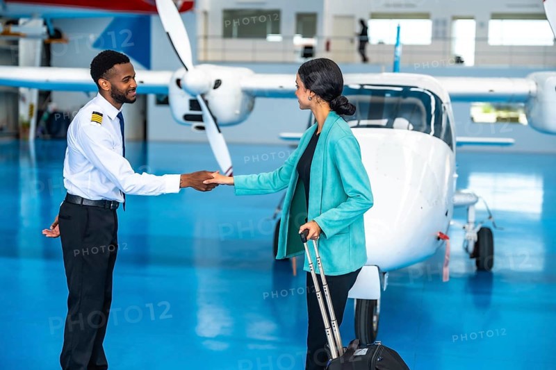 Pilot and businesswoman shaking hands in front of a private jet inside a hangar, finalizing their partnership before departure