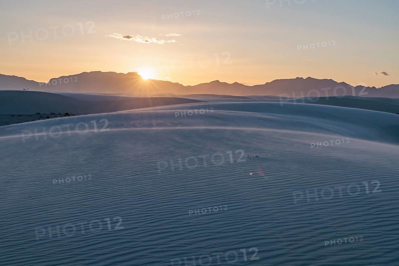 Rays of light over the mountains highlight windblown sand at sunset at White Sands National Park in Alamogordo, New Mexico, USA, North America