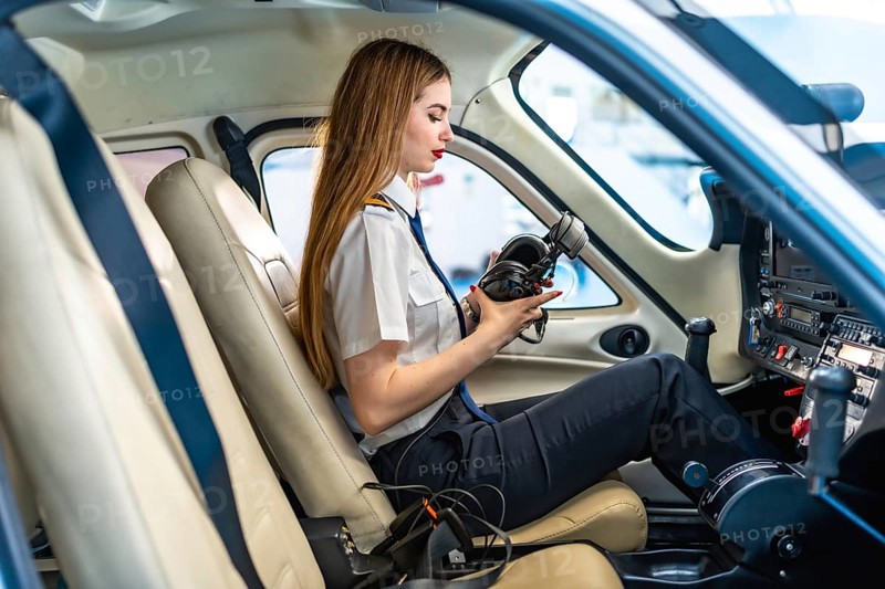 Young woman pilot checking her headset while sitting in the cockpit of a small aircraft, preparing for flight