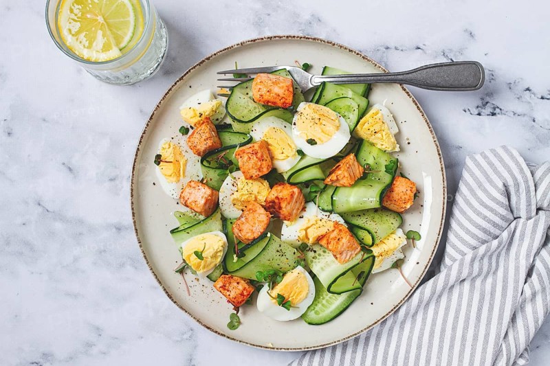 Delicious salmon and egg salad served on a plate with fresh cucumber and herbs for a healthy meal at lunchtime