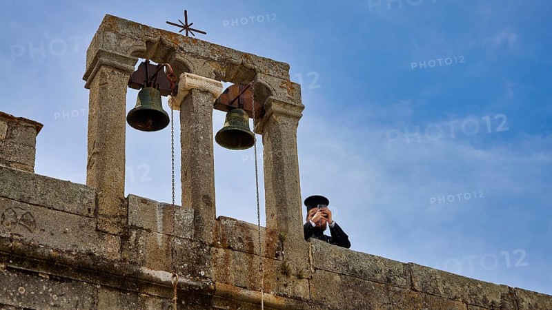 Priest next to bells on a wall in front of a blue sky, Monastery of St John the Theologian, Monastery of St John the Theologian, World Heritage Site 1999, Patmos, Dodecanese, Greek Islands, Greece, Europe