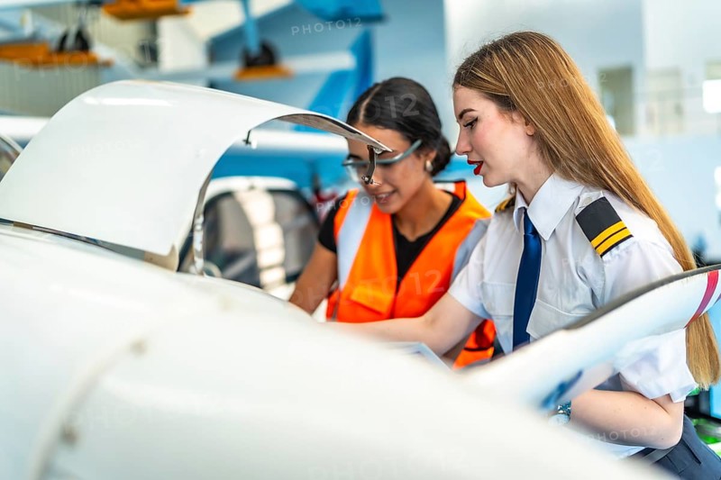 Female pilot and an aircraft maintenance engineer are inspecting the engine of a small plane in a hangar