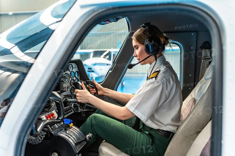 Confident female pilot wearing headset and holding steering wheel while sitting in cockpit of airplane