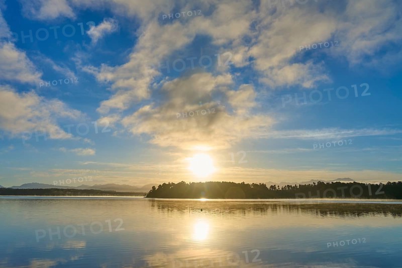 Sunlight breaks through the clouds in the morning over a calm lake, Lake Mahinapua, Ruatapu, South Island, New Zealand, Oceania