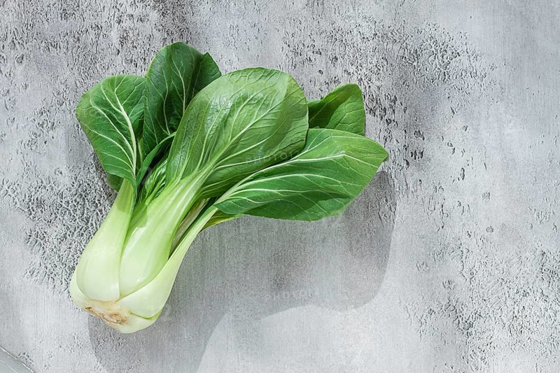 Fresh bok choy, laid out on a light gray surface, top view, natural light