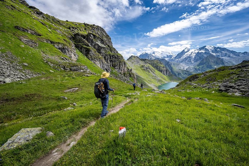 Mountaineer on hiking trail in mountain landscape, descent from Col du Louvie, view of Lac du Louvie and glaciated mountain peaks of the Grand Combine, Valais Alps, Val de Bagnes, Valais, Switzerland, Europe