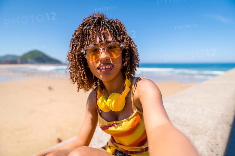 Tourist enjoying summer holidays at the beach, capturing a joyful selfie while soaking up the sun, surrounded by ocean waves and sandy shores