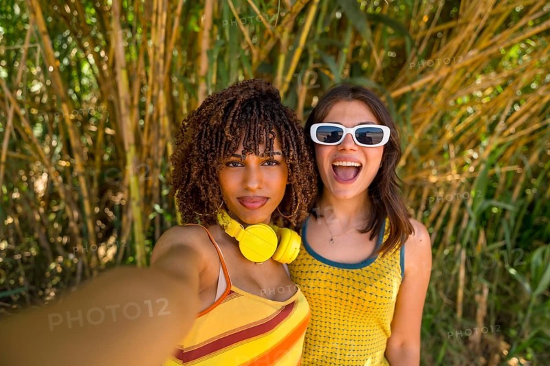 Two cheerful female friends capturing a joyful selfie while enjoying their vacation in a lush bamboo forest, surrounded by vibrant greenery