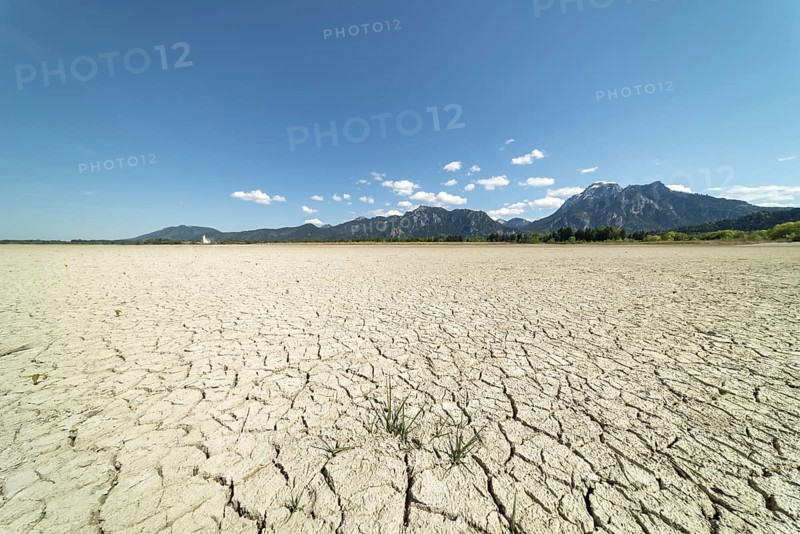Cracked, dried out ground, waterless Forggensee in spring, behind it Tegelberg massif and Säuling, Ammergau Alps, near Füssen, Ostallgäu, Bavaria, Germany, Europe